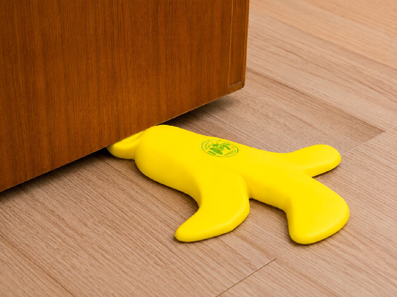 Sujetapuertas divertido de silicona con forma de platano amarillo chafado debajo de una puerta en casa