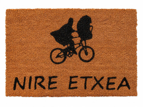 Felpudo de fibra de coco con la silueta negra de E.T. y Elliot volando en bicicleta frente a la luna y la frase Nire Etxea